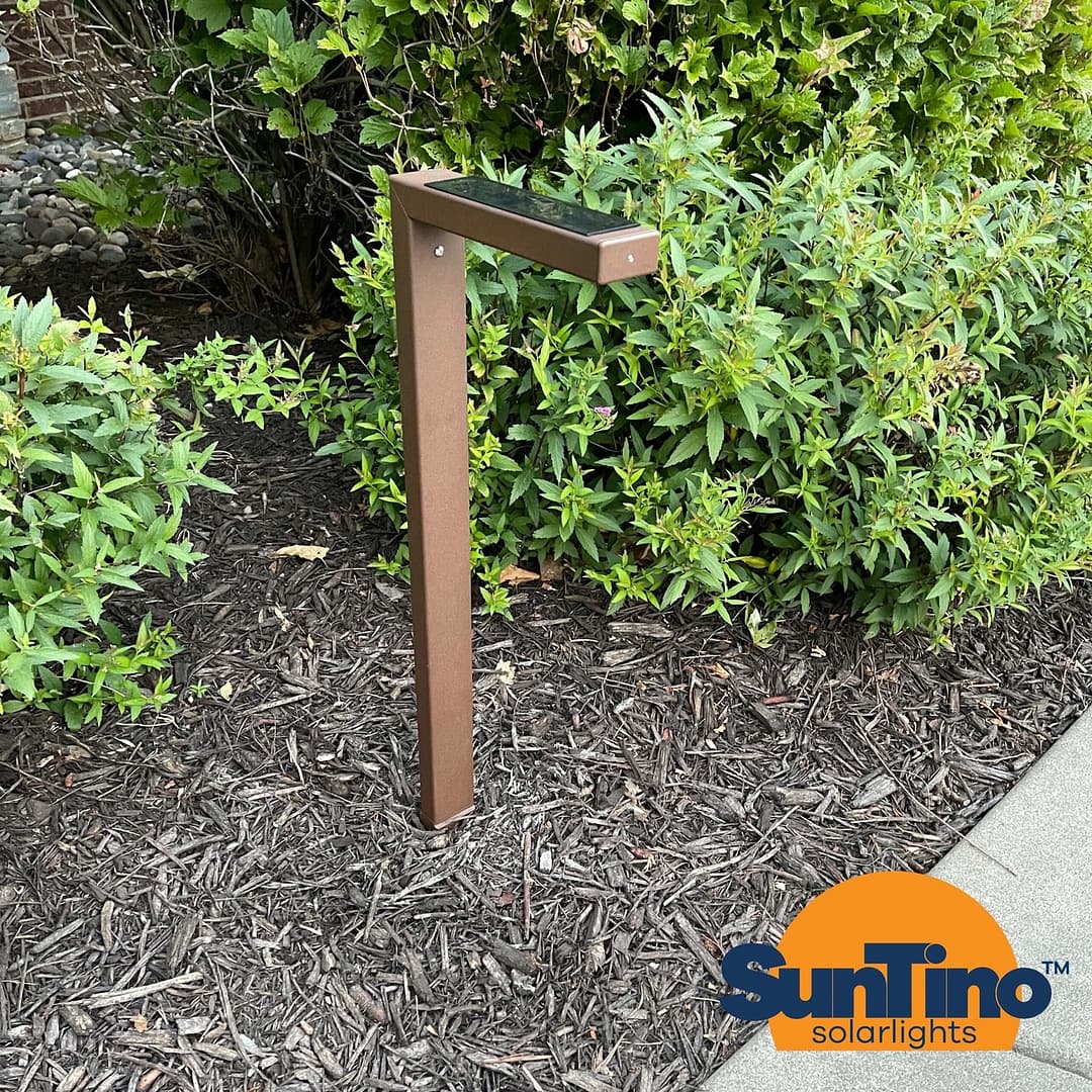 A metal post with a solar light in front of some shrubs.