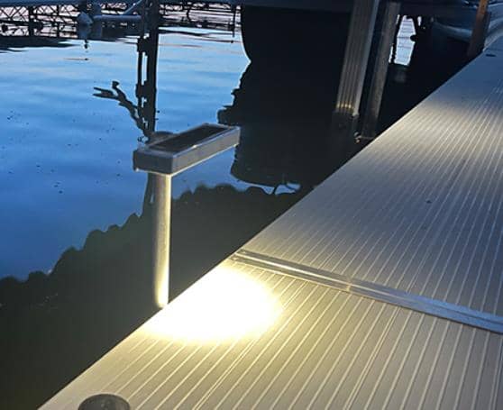 A dock with a light on it next to a body of water illuminated by solar lighting.